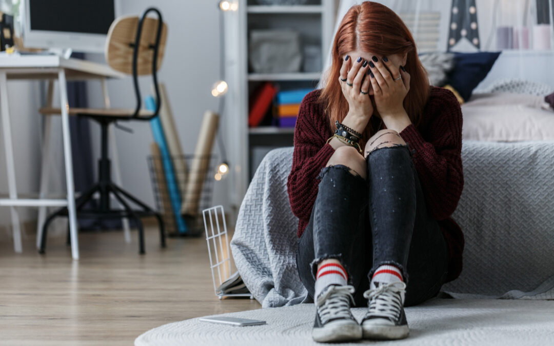 Eine jugendliche Personmit schwarz lackierten Fingernägeln schlägt die Hände vor ihr Gesicht und hadert mit der Welt